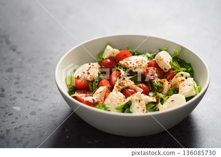 Salad with cherry tomatoes, mozzarella and frisee leaves in white bowl on concrete background 136085730