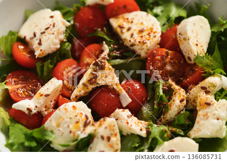 Closeup salad with cherry tomatoes, mozzarella and frisee leaves in white bowl on concrete background 136085731