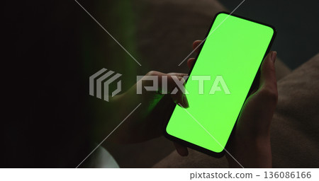 Young woman sitting on a couch and using smartphone with green screen Young woman sitting on a couch and using smartphone with green screen 136086166
