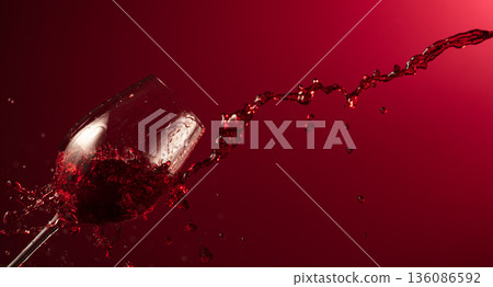 Glass and red wine splash on a dark red background. Glass and red wine splash on a dark red background. 136086592