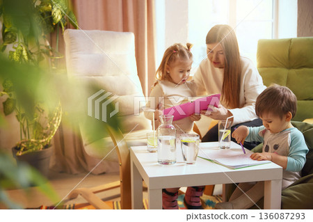 Children drawing and reading at table with mother at home. Children drawing and reading at table with mother at home. 136087293