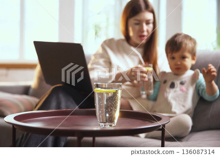 Mother and toddler drinking water with lemon at home. Mother and toddler drinking water with lemon at home. 136087314