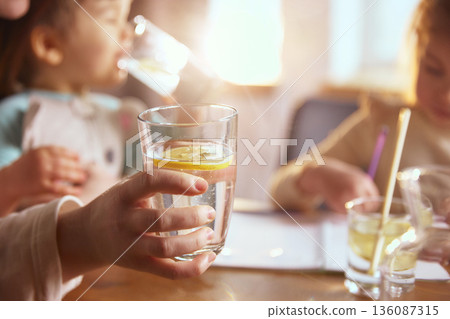 Glass of water with lemon during kids drawing at home table. Glass of water with lemon during kids drawing at home table. 136087315