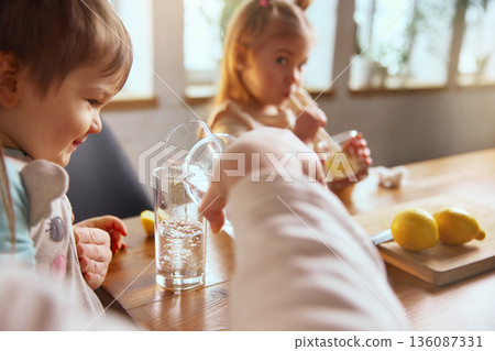 Child learning to drink water with lemon at table. 136087331