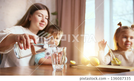 Mother pouring fresh water for children at home table Mother pouring fresh water for children at home table 136087335