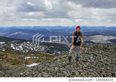 Man hiker standing on rocky mountain top looking at scenic winter landscape. Adventure travel and exploration concept for nature photography. Man hiker standing on rocky mountain top looking at scenic winter landscape. Adventure travel and exploration concept for nature photography. 136088958
