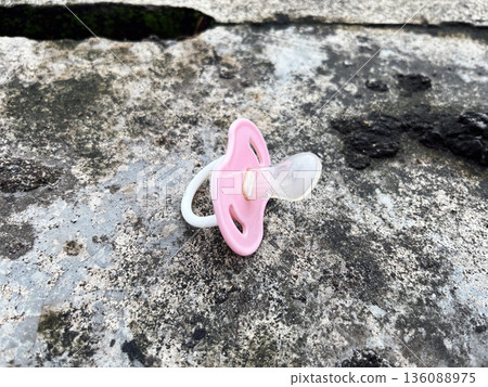 forgotten pink baby pacifier lies on a rough weathered concrete surface, evoking feelings of nostalgia, abandonment, or the passage of time forgotten pink baby pacifier lies on a rough weathered concrete surface, evoking feelings of nostalgia, abandonment, or the passage of time 136088975