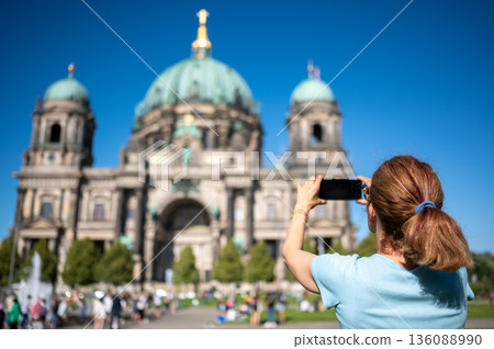 Berlin, germany, august 11, 2023. Woman traveler photographing berlin cathedral with smartphone on sunny summer day, blue sky and historic cityscape behind her 136088990