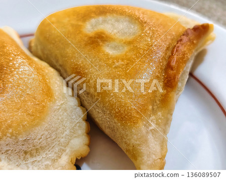 Two warm pastries with a golden brown crust are placed on a white plate in a home kitchen. The pastries are freshly baked and ready to be enjoyed 136089507