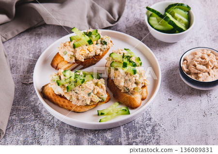 Cod liver, egg, cucumber salad on toast on a plate on the table Cod liver, egg, cucumber salad on toast on a plate on the table 136089831