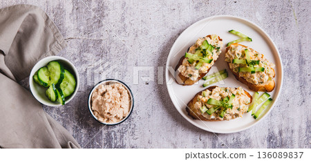 Cod liver, egg, cucumber salad on toast on a plate on the table top view web banner 136089837