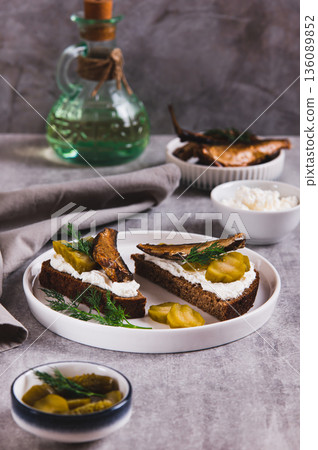Sandwiches with ricotta, pickles and sprats on rye bread on a plate on a table vertical view Sandwiches with ricotta, pickles and sprats on rye bread on a plate on a table vertical view 136089852