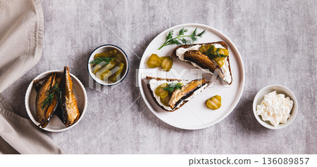 Rye bread toasts with cream cheese, sprats and pickles on a plate on the table top view web banner 136089857