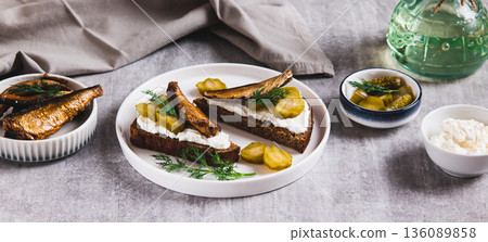 Sandwiches with ricotta, pickles and sprats on rye bread on a plate on a table web banner 136089858