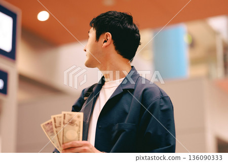 A man holding cash in front of a ticket machine. Photo courtesy of Kansai International Airport (KIX) 136090333