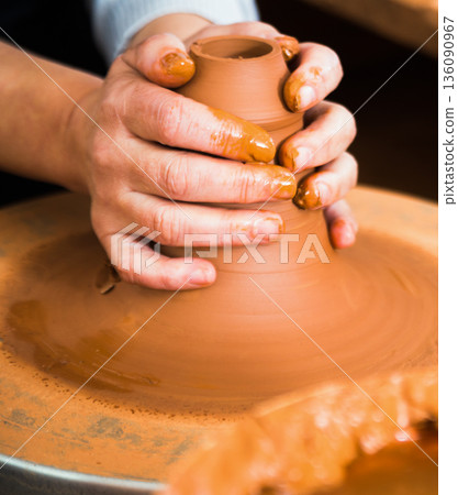 Hands of artisan forming clay shape on turning pottery wheel 136090967