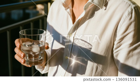 Person in White Shirt Holding a Cold Glass of Water with Ice 136091531
