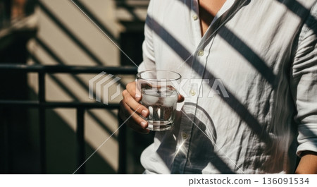 Person in White Shirt Holding a Cold Glass of Water with Ice 136091534