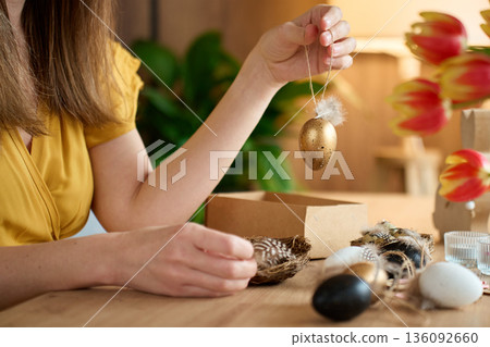 Woman holding handmade golden Easter egg ornament with feathers Woman holding handmade golden Easter egg ornament with feathers 136092660
