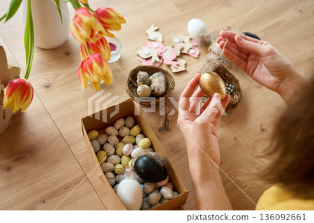 Woman decorating handmade Easter eggs with feathers at home Woman decorating handmade Easter eggs with feathers at home 136092661