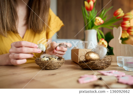 Woman decorating nest with speckled Easter eggs and feathers Woman decorating nest with speckled Easter eggs and feathers 136092662