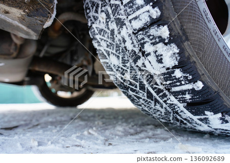 Winter car tire with snow on tread on icy road 136092689