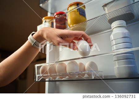 Hand taking egg from refrigerator door shelf 136092731
