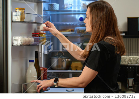 Woman taking egg from open refrigerator 136092732