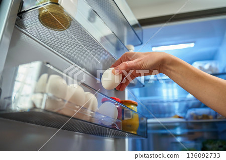 Hand taking egg from refrigerator door shelf 136092733