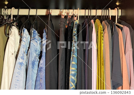 Assortment of clothes hanging in a dark wardrobe 136092843