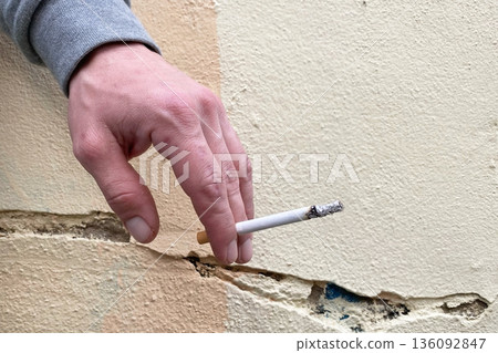 Hand holding a lit cigarette against a cracked, textured wall Hand holding a lit cigarette against a cracked, textured wall 136092847