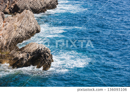 Rugged coastal rocks rise from the deep blue sea 136093106