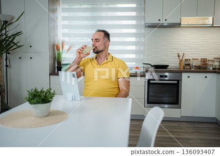 Man drinking healthy beverage using tablet for breakfast 136093407