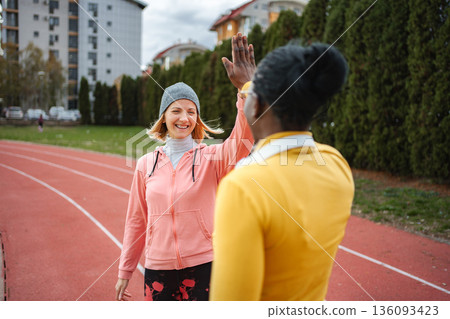 Diverse women friends high-fiving on a running track 136093423