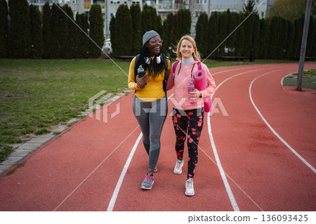 Diverse women friends walking together on running track 136093425