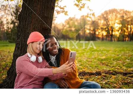 Diverse friends taking a selfie using smartphone in autumn park Diverse friends taking a selfie using smartphone in autumn park 136093436