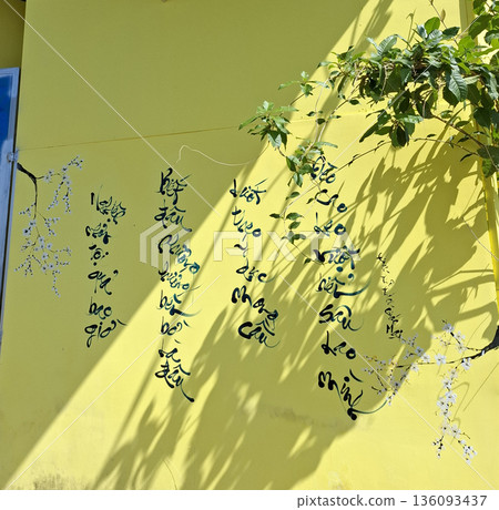 Yellow wall with Vietnamese calligraphy and leaf shadows background Yellow wall with Vietnamese calligraphy and leaf shadows background 136093437