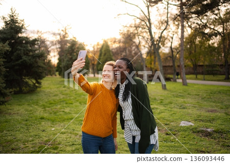 Diverse women friends taking selfie in park laughing together 136093446