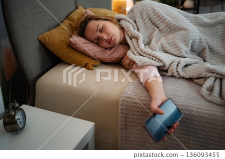 Woman sleeping soundly in bed with phone in hand Woman sleeping soundly in bed with phone in hand 136093455