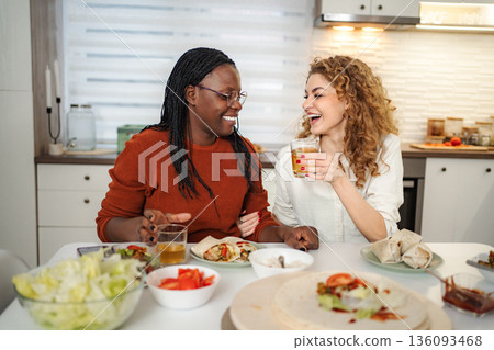Diverse couple laughing enjoying a meal together in kitchen 136093468