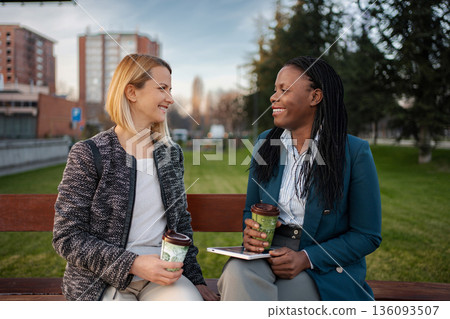 Diverse women colleagues enjoying coffee break in city park Diverse women colleagues enjoying coffee break in city park 136093507
