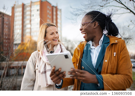 Diverse businesswomen laughing enjoying digital tablet outdoors Diverse businesswomen laughing enjoying digital tablet outdoors 136093508