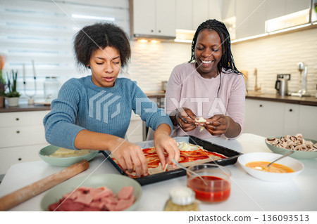 African American mother and daughter preparing pizza together in kitchen African American mother and daughter preparing pizza together in kitchen 136093513