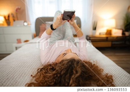 Woman relaxing in bed messaging on smartphone social media 136093553