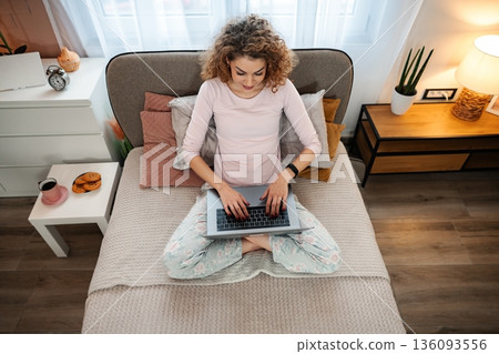 Young woman working remotely on laptop in bed Young woman working remotely on laptop in bed 136093556