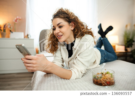 Young woman relaxing in bed using smartphone at home 136093557