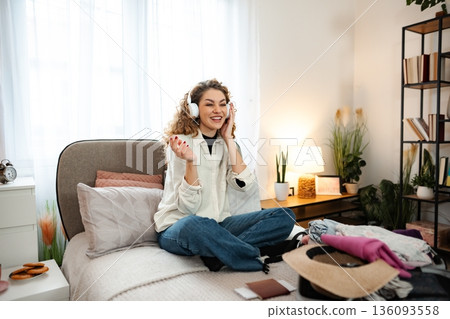 Young adult woman listening to music packing for travel Young adult woman listening to music packing for travel 136093558