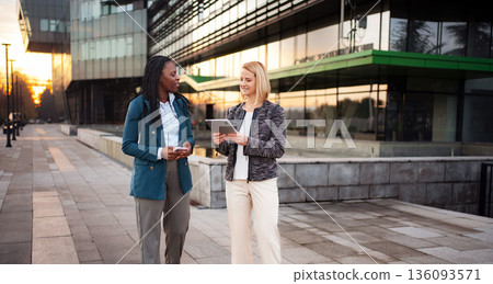 Diverse businesswomen walking, discussing work with tablet and smartphone 136093571