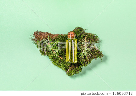 Glass essential juniper oil bottle placed on green moss with small branches. View from above. Glass essential juniper oil bottle placed on green moss with small branches. View from above. 136093712
