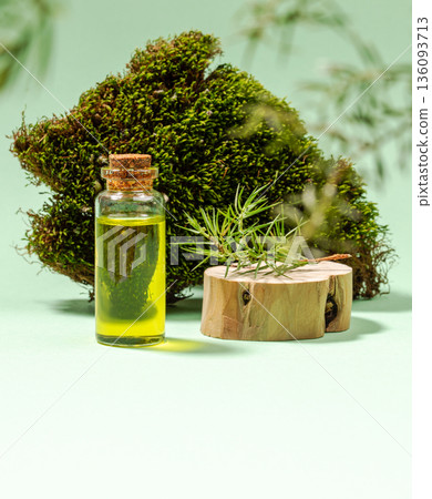 Glass bottle of essential juniper oil with wooden base and moss background on green. Copy space. Glass bottle of essential juniper oil with wooden base and moss background on green. Copy space. 136093713